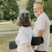 Zwei ältere Personen gehen auf der Wiese und halten eine Turnmatte